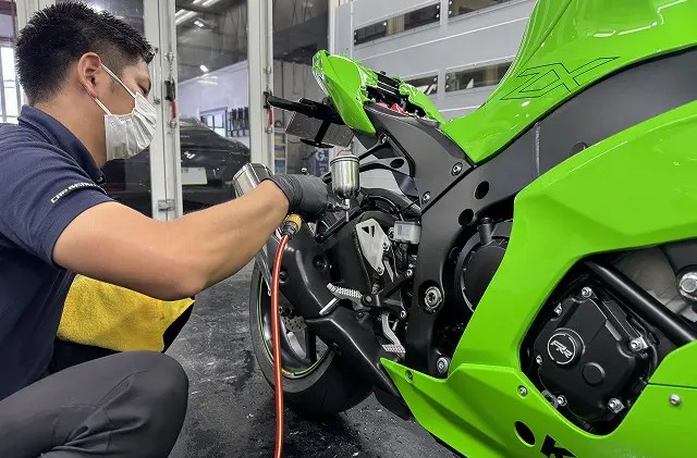 ガンスプレーでエンジン回りにコーティング剤を吹きかけている様子