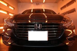 Front view of a black Honda sedan in a brightly lit garage with orange-tinted lights and a blurred license plate
