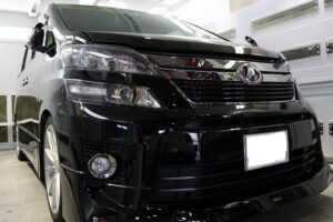 Front view of a shiny black minivan in a showroom, showing the grille, headlights, and emblem