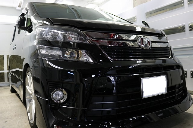 Front view of a shiny black minivan in a showroom, showing the grille, headlights, and emblem