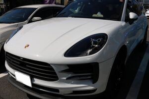 White Porsche SUV parked in a lot, angled from the front-left showing the emblem and grille.