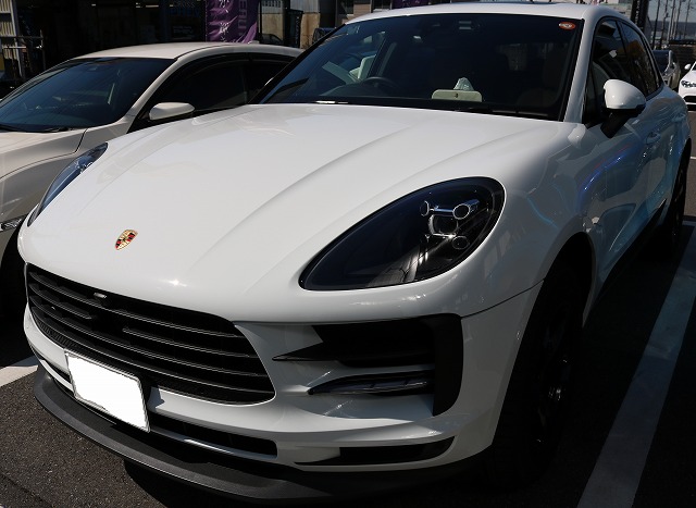 White Porsche SUV parked in a lot, angled from the front-left showing the emblem and grille.