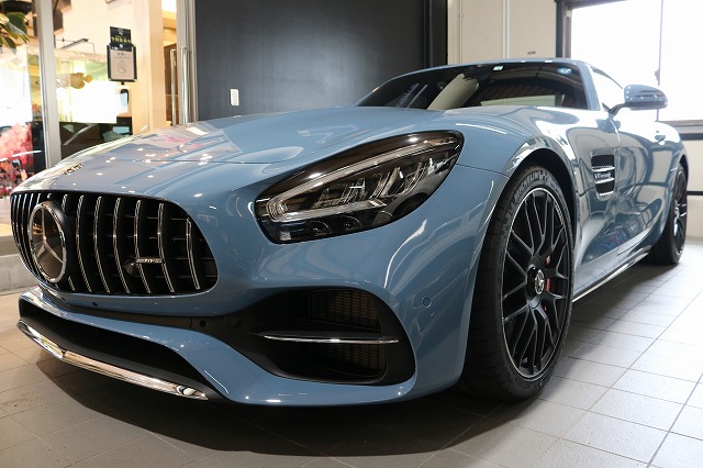 Blue Mercedes-Benz AMG GT sports car displayed in a showroom, front-angled view showing grille and large wheels