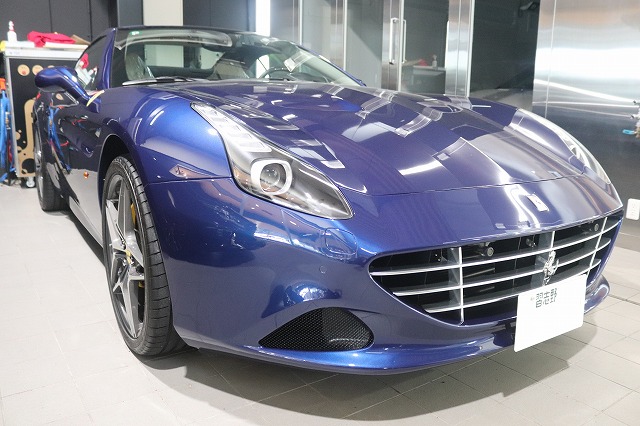 Front view of a blue convertible sports car in a showroom, showing its grille, headlights, and glossy finish.