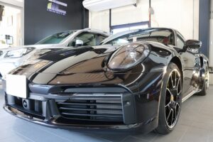Low-angle view of a glossy black Porsche on a showroom floor, front bumper and large wheels visible.