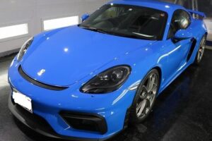 Blue Porsche two-door sports car in a showroom, shown from front-side angle with sleek curves and large wheels.