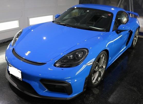 Blue Porsche two-door sports car in a showroom, shown from front-side angle with sleek curves and large wheels.