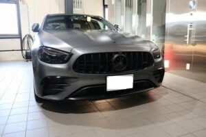Front view of a gray Mercedes-Benz SUV in a dealership showroom, license plate blurred, showing the distinctive grille and emblem.