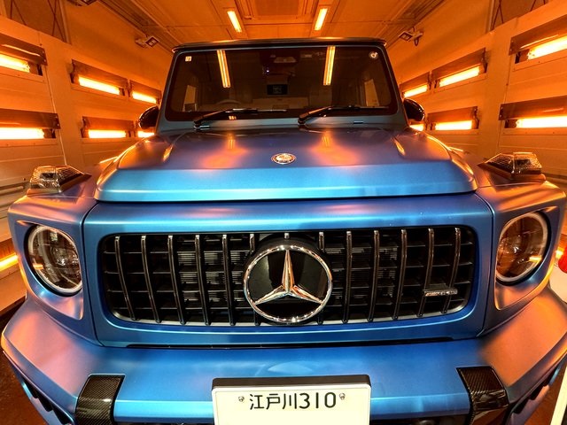Front view of a metallic blue Mercedes truck in a brightly lit orange-toned tunnel, grille and emblem centered, Japanese license plate visible at the bumper.