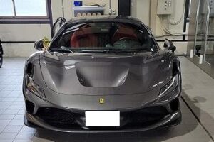 Front view of a gray Ferrari sports car in a showroom, red interior visible through the windshield, distinctive emblem on the hood.
