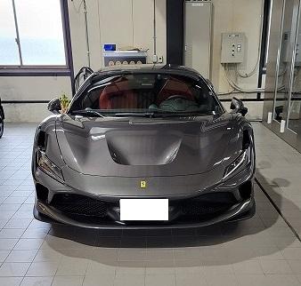 Front view of a gray Ferrari sports car in a showroom, red interior visible through the windshield, distinctive emblem on the hood.