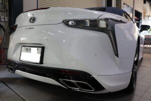 White Lexus LC 500 convertible seen from the rear in a showroom, highlighting quad exhausts and sleek taillights, with a visible Lexus logo and license plate area at the back