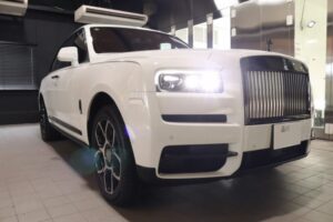White luxury SUV in a showroom, front three-quarter view showing a prominent chrome grille and bright headlights