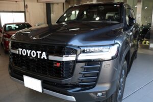 Front three-quarter view of a dark gray Toyota pickup truck on showroom flooring, highlighting the bold grille with TOYOTA lettering and LED headlights.