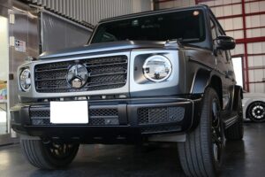 Front-left view of a metallic gray Mercedes-Benz G-Class SUV parked indoors, showing its signature round headlights and prominent grille.