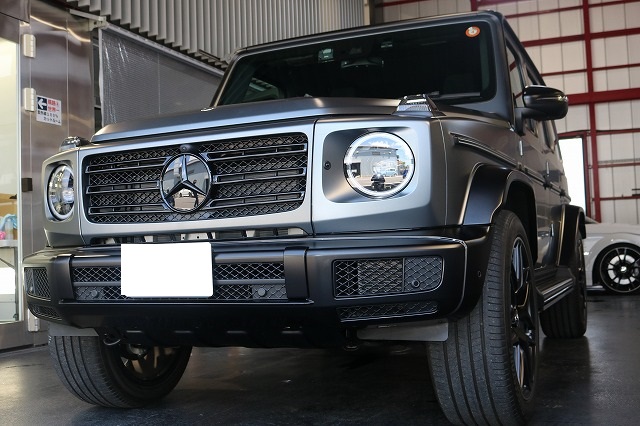 Front-left view of a metallic gray Mercedes-Benz G-Class SUV parked indoors, showing its signature round headlights and prominent grille.