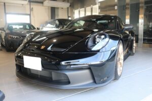 Front view of a sleek black Porsche sports car on display in a showroom, glossy finish and low stance visible with other cars in the background