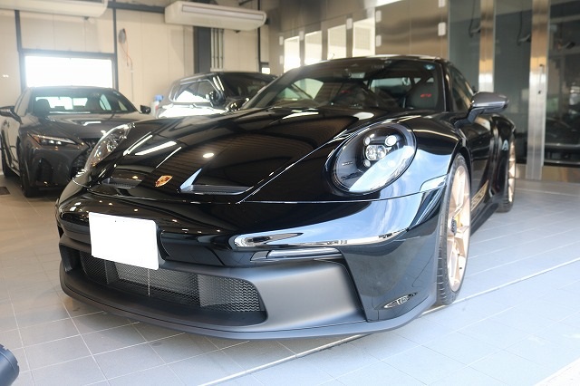 Front view of a sleek black Porsche sports car on display in a showroom, glossy finish and low stance visible with other cars in the background