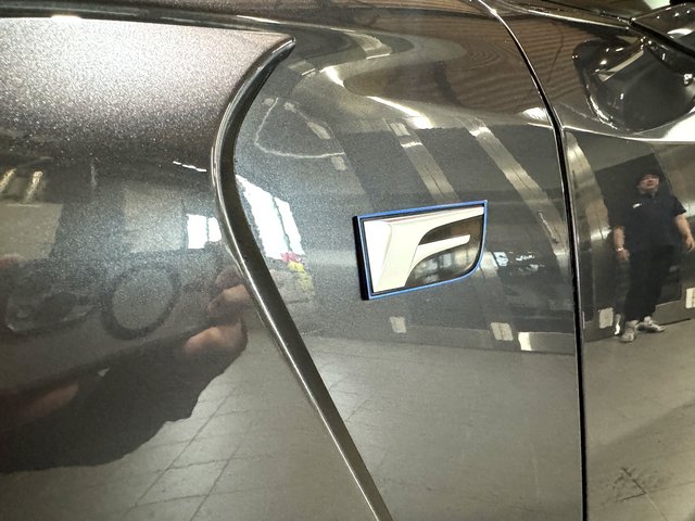 Close-up of a metallic gray car side panel with a blue-bordered badge ornamented near the seam between panels.