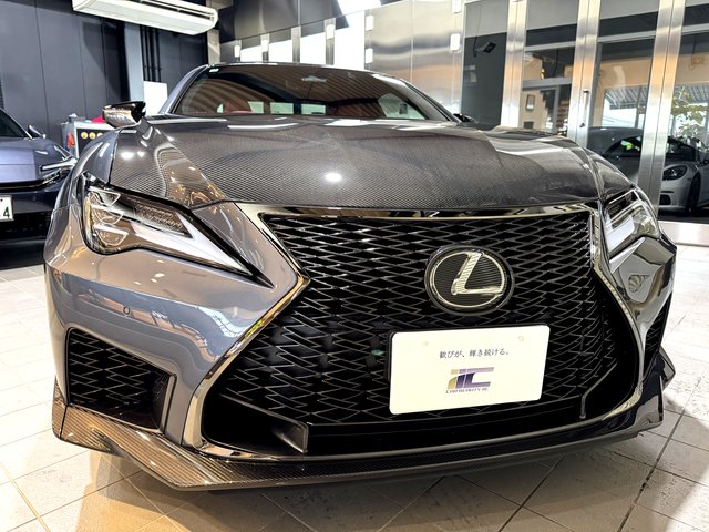 Front view of a dark gray Lexus sedan with a large spindle grille in a showroom that highlights its aggressive styling.