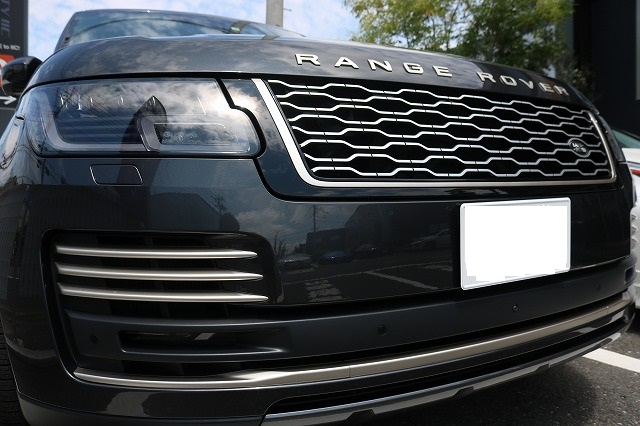 Close-up of a dark Range Rover's front end, showing the grille, headlight, and a blanked license plate.