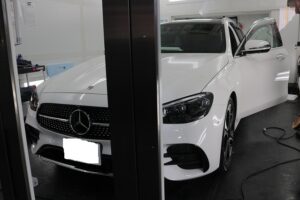 IMG_6828 - トータルカービューティIIC White Mercedes-Benz sedan in a service bay, driver's door open and tools nearby in a workshop setting.