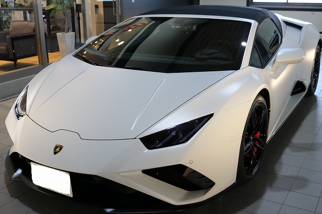 White Lamborghini convertible on a showroom floor, angled front-left with a black soft top and red brake calipers visible on the wheels