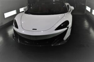 IMG_9274 - トータルカービューティIIC White high-performance sports car with a low, curved front, parked in a showroom bay.